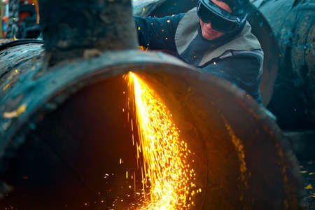 The welder sits near the pipe and cuts it with the help of cetylene welding. A worker on the street...
