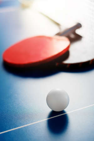 Two tennis rackets and a white ball lie on a tennis table near the net. Sports background.の写真素材