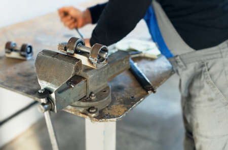 A worker in overalls works behind a workbench with metal vises. Production of metal parts at the factory. Equipment assembly.の写真素材