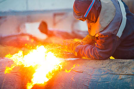 The welder cuts large metal pipes with ocetylene welding. A worker on the street cuts large-diameter...