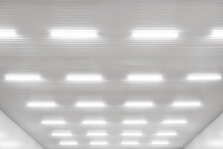 Many LED industrial lamps hang on white ceiling in production hall or hangar and shine bright light....
