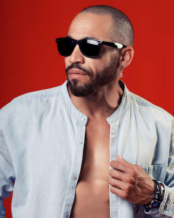 Confident sexy man in shirt and sunglasses poses on red background. Promotional background casual...