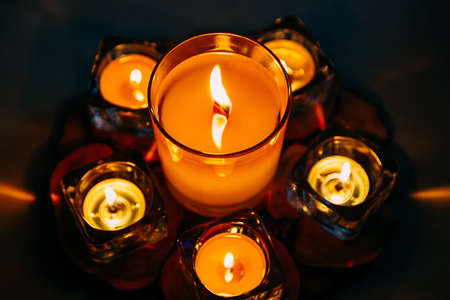 Large wax candle in glass candlestick burns among small flat candles. View from above. Relaxation...