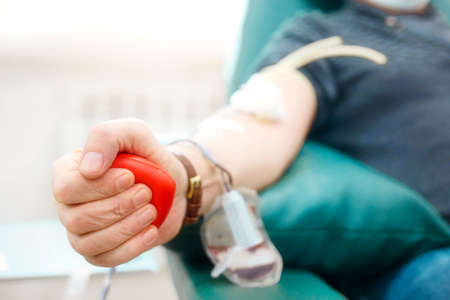 Topic of donation. Man donates blood in hospital. Mans hand squeezes rubber heart. Close-up. Donor...