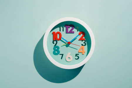 Photos of round childrens wall clocks with multi-colored numbers on blue background with shade. Top...