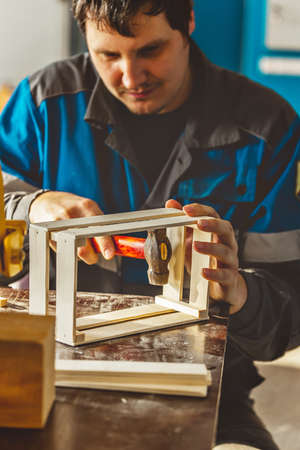 Young Caucasian carpenter in working clothes makes wooden boxes in carpentry workshop. Real scene. Workflow. Small business. Environmentally friendly packaging and containers.の写真素材