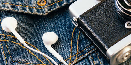 Film camera and white wired headphones lie against background of denim. Fashionable hipster background. Retro style. Photographers Day. Top viewの写真素材