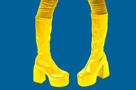 Womens feet in gold boots with high soles on blue background. Promotional photo of fashionable...
