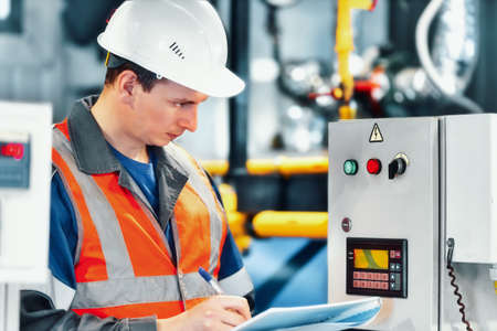 Young engineer to helmet and protective vest records in log readings of devices or gas consumption...