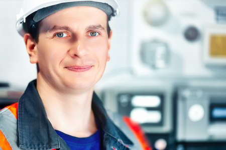 Young positive engineer in helmet and construction vest looks into camera and smiles. Portrait of...