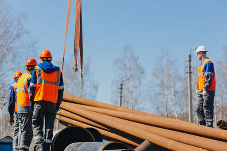 Group of slingers in construction helmets and vests on street unload metal pipes. Real scene....