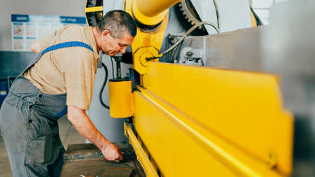Worker cuts metal sheets on mechanical guillotine machine in production hall. Industrial equipment...