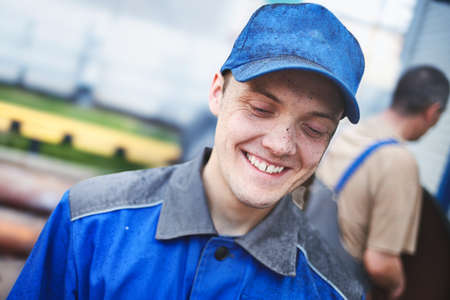Portrait of young worker in work clothes and blue baseball cap with stained face. Cheerful and happy...