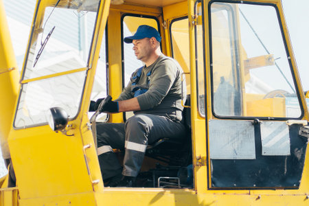 Middle-aged man sits in cab of tractor and works. Portrait of worker in open cab of truck tractor or...