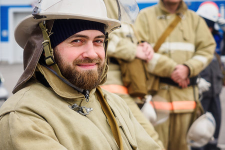 Portrait of bearded rescuer on summer day on street. Firefighter in protective uniform and helmet looks into camera and smiles. Authentic Caucasian rescue worker. Positive emotions..の写真素材