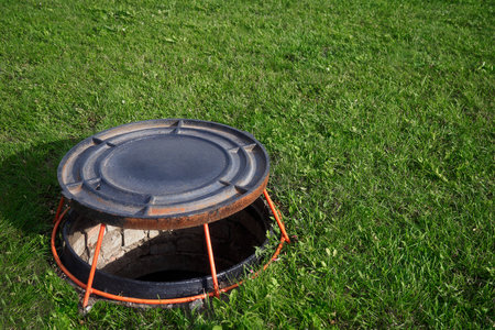 Open well hatch on green lawn. Manhole cover is on stand. Device for ventilation of wells..