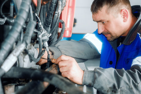 Car mechanic repairs large truck or tractor in workshop. Professional mechanic repairs truck engine. Genuine worker..の写真素材