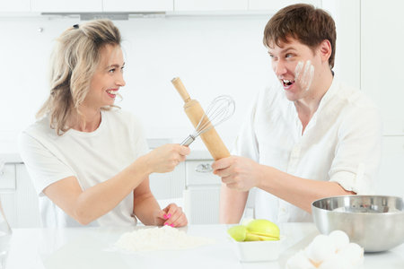 Husband and wife quarrel in kitchen while cooking. Comic and cheerful confrontation between man and woman in kitchen. Background..の写真素材