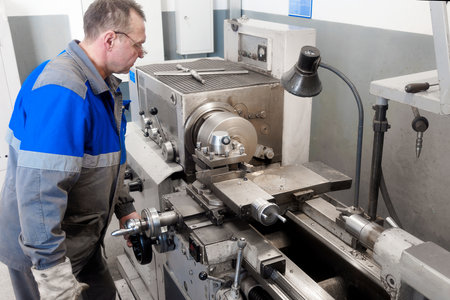Adult turner of 50-55 years old works in workshop behind lathe. Industrial production of metal...