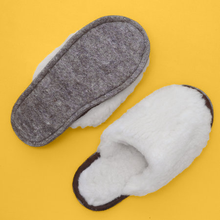 Room slippers made of white wool and felt lie on yellow background. View from top..の写真素材