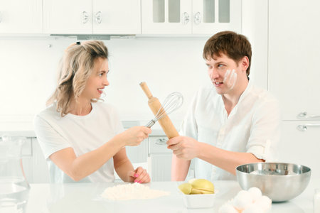 Husband and wife quarrel in kitchen while cooking. Comic and cheerful confrontation between man and woman in kitchen. Background..の写真素材