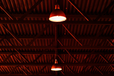 Gloomy red lighting in industrial hangar. Industrial luminaires or lampshades hang under roof inside production hall. Background..の写真素材