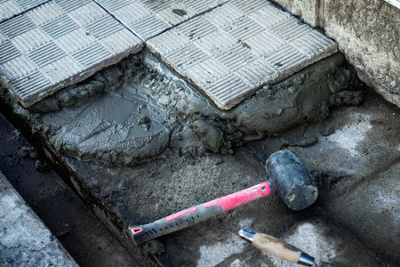 Construction and repair of buildings. Tile lies in cement on sidewalk next to hammer.の写真素材