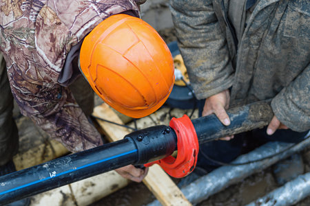 Worker in helmet repairs communal water pipe in trench on street. Work of public utilities to eliminate accident. Replacement of old water supply pipes. Authentic workflow. Real people..の写真素材