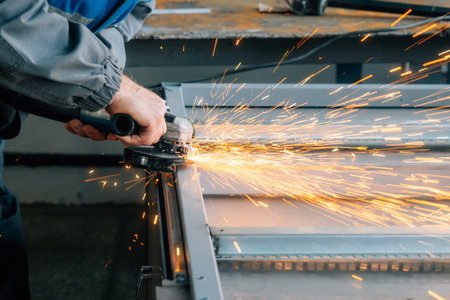 Hands of worker with close-up grinder during workflow. Man grinds grinder metal profile in shop and sparks fly. Authentic workflow behind workbench in production room..の写真素材