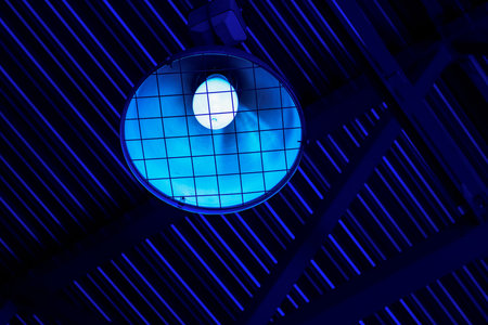Lampshade with lamp hangs under roof of industrial room inside. Gloomy blue light in production hall or abandoned warehouse..の写真素材
