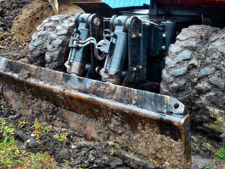 Wheeled tractor with shovel clears ground on cloudy rainy day. Dirty bulldozer shovel close-up..の写真素材