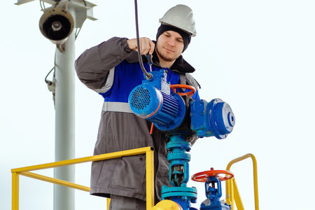 A Caucasian man in work clothes with a screwdriver is repairing an industrial equipment engine...
