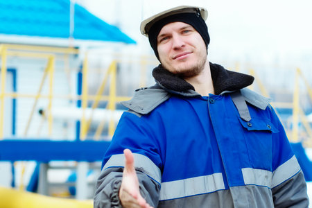 Invitation to team of professional gas workers. Young gas engineer in hardhat and winter pea coat extends his hand forward to greet. Positive attitude. Authentic Caucasian worker.の写真素材