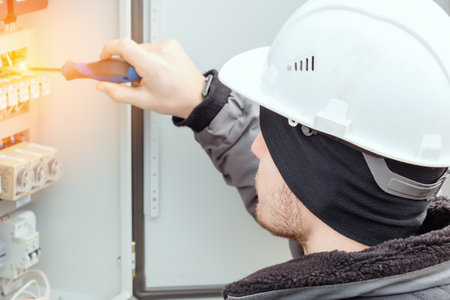Close-up portrait of energy engineer in hard hat at work. Electrician or instrumentation fitter carries out repairs and diagnostics of equipment in electrical cabinet.の写真素材
