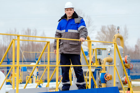 Portrait of worker in white helmet and winter pea jacket at industrial gas facility. Middle-aged Caucasian man stands in full growth on territory of gas distribution station. Genuine worker.の写真素材