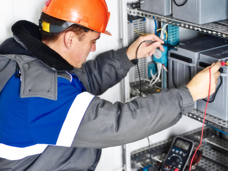 Electrician in helmet or instrumentation fitter checks capacity of batteries of automatic control system of gas distribution station with multimeter.の写真素材