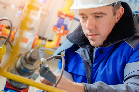 Close-up portrait of worker in hard hat and winter overalls. Authentic workflow. Gas equipment repairman at work. Professional diagnostics and adjustment of equipment.の写真素材