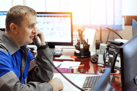 Telephone line operator answers phone and looks at computer monitor. Middle-aged Caucasian dispatcher at work. Authentic workflow. Side view with copy space.の写真素材