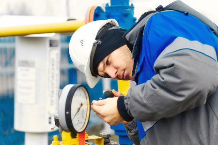 Mechanic of instrumentation and automation carefully inspects gas pressure gauge outside at gas distribution station. Authentic workflow.の写真素材