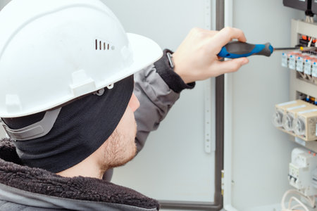 Close-up portrait of energy engineer in hard hat at work. Electrician or instrumentation fitter carries out repairs and diagnostics of equipment in electrical cabinet.の写真素材