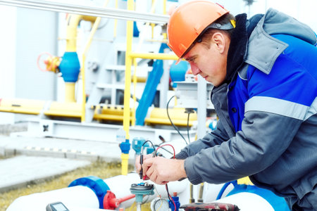 Mechanic of instrumentation and automation diagnoses sensors on the pipes of a gas distribution station with a multimeter in winter. Professional inspection and diagnostics of the working condition of gas equipment. Photo of a real workflow.の写真素材