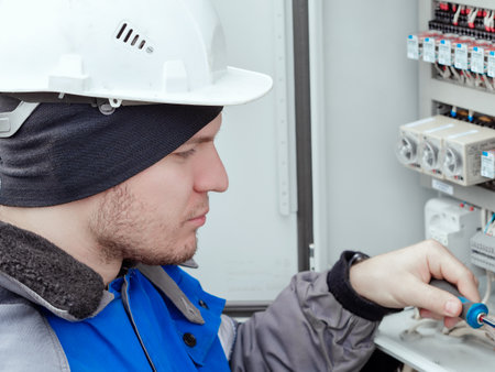 Close-up portrait of energy engineer in hard hat at work. Electrician or instrumentation fitter carries out repairs and diagnostics of equipment in electrical cabinet.の写真素材