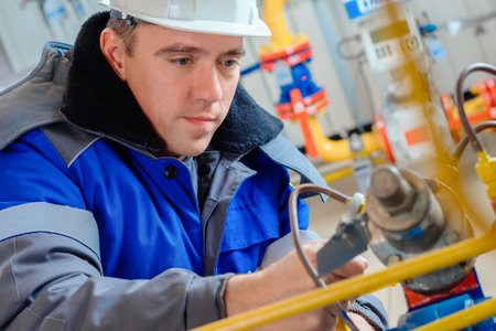 Close-up portrait of worker in hard hat and winter overalls. Authentic workflow. Gas equipment repairman at work. Professional diagnostics and adjustment of equipment.の写真素材