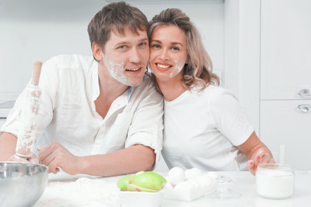 Portrait of young Caucasian family couple in kitchen. Husband and wife soiled in flour look at camera and smile. Happy husband and wife are preparing festive dinner together.の写真素材