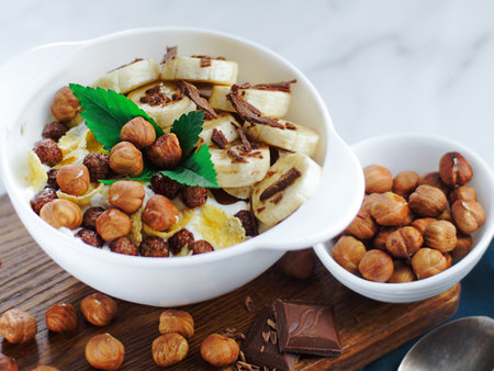 Banana salad with chocolate and hazelnuts in yogurt in a white plate. View from above. Healthy nutritious breakfast.の写真素材