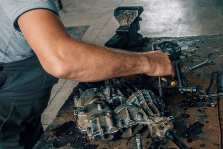 Mechanic repairs gearbox on metal workbench in car repair shop. Auto mechanic at work. Authentic workflow. Close-up hands.の写真素材