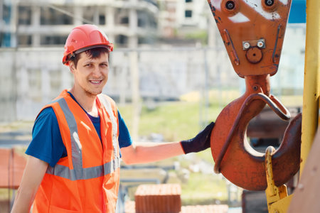 Portrait of young builder in construction helmet and flare vest on summer day at construction site....