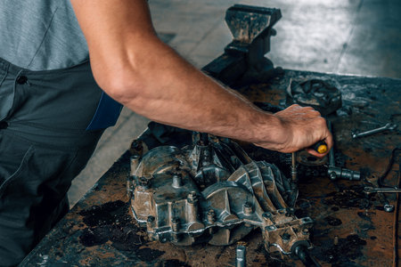 Mechanic repairs gearbox on metal workbench in car repair shop. Auto mechanic at work. Authentic workflow. Close-up hands.の写真素材