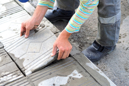 Worker tiler lays tiles with cement outside on summer day. Authentic workflow. Hands with facing tiles.の写真素材