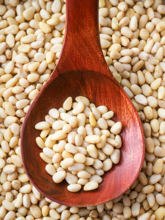 Cleaned pine nuts. Pine nut kernels lie in wooden spoon. Top view of nuts close-up. Advertising photography for marketplaces or online stores.の写真素材